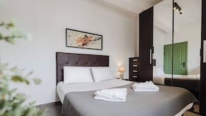 Habitación de hotel con una cama grande, una mesita de noche con lámpara, una puerta verde y un cuadro en la pared.