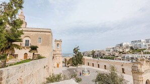 Un edificio histórico con una torre de campanas, un patio y vistas al mar.