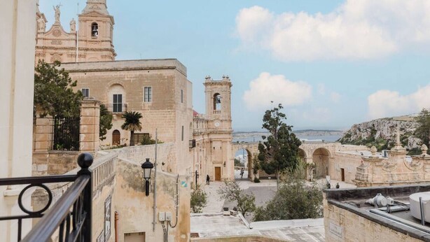 Un edificio histórico con una torre de campanas y arcos, con vistas a la costa.