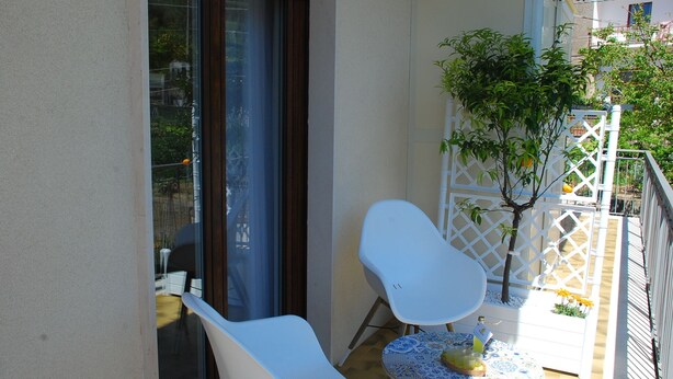 A balcony with a white chair, a small table with a blue and white patterned tablecloth, and a potted plant. - OrangeSun Holiday Home x5 with parking (Massa Lubrense)