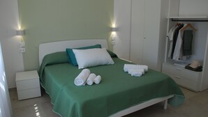 A neatly made bed with green bedding and white pillows, a bedside table with a lamp, and a wardrobe with hanging clothes. - OrangeSun Holiday Home x5 with parking (Massa Lubrense)