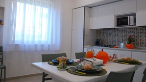 A modern kitchen with white cabinets, a microwave, and a patterned backsplash. There is a dining table set with plates, glasses, and a fruit bowl. - OrangeSun Holiday Home x5 with parking (Massa Lubrense)