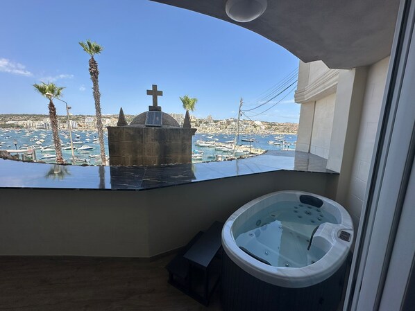 Un balcón con vista a un puerto deportivo, un jacuzzi y una estructura de piedra con una cruz.