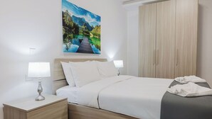 A neatly arranged hotel room with a bed, bedside lamps, a nightstand, a wardrobe, and a painting of a landscape on the wall. - This apartment is a 1 bedroom(s), 1 bathrooms, located in San Pawl il-Baħar, null. (San Pawl il-Baħar)