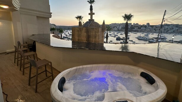 A hot tub with a digital interface, a seating area with chairs, and a view of a marina with boats and palm trees. - This apartment is a 1 bedroom(s), 1 bathrooms, located in San Pawl il-Baħar, null. (San Pawl il-Baħar)