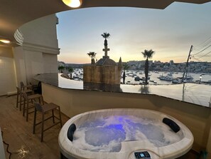 Un jacuzzi con control digital, una zona de estar con sillones y vistas a un puerto deportivo con barcos y palmeras.