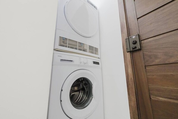 A white stacked washer and dryer unit mounted on a wall, with a wooden door to the right.