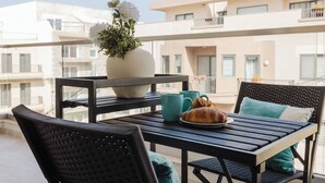 Varanda com mesa posta para o café da manhã, incluindo croissants e xícaras de café, além de um vaso grande com flores.