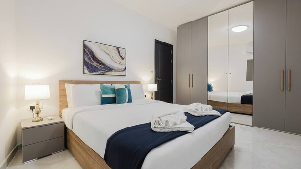 Quarto de hotel moderno com uma cama grande, mesas de cabeceira com abajures, um guarda-roupa e um espelho amplo.