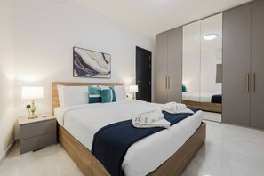 A modern hotel room with a large bed, bedside tables with lamps, a wardrobe, and a large mirror.
