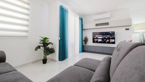 Uma sala de estar moderna com sofás cinzas, uma TV de tela plana na parede e um vaso com planta.