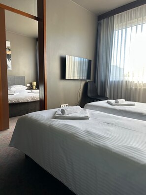 A hotel room with two beds, a flat-screen TV, and a large window with sheer curtains. - Hotel Vento (Ventspils)
