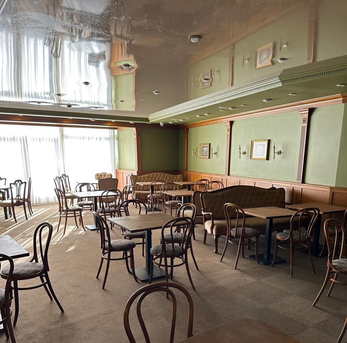 Un restaurante con cabinas y mesas, paredes verdes y cuadros enmarcados.