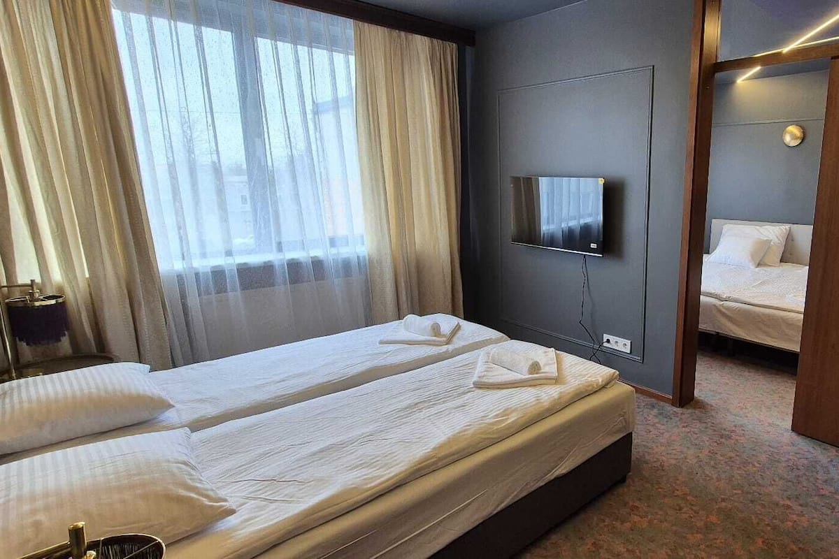 A hotel room with two beds, a TV mounted on the wall, and a door leading to another room.