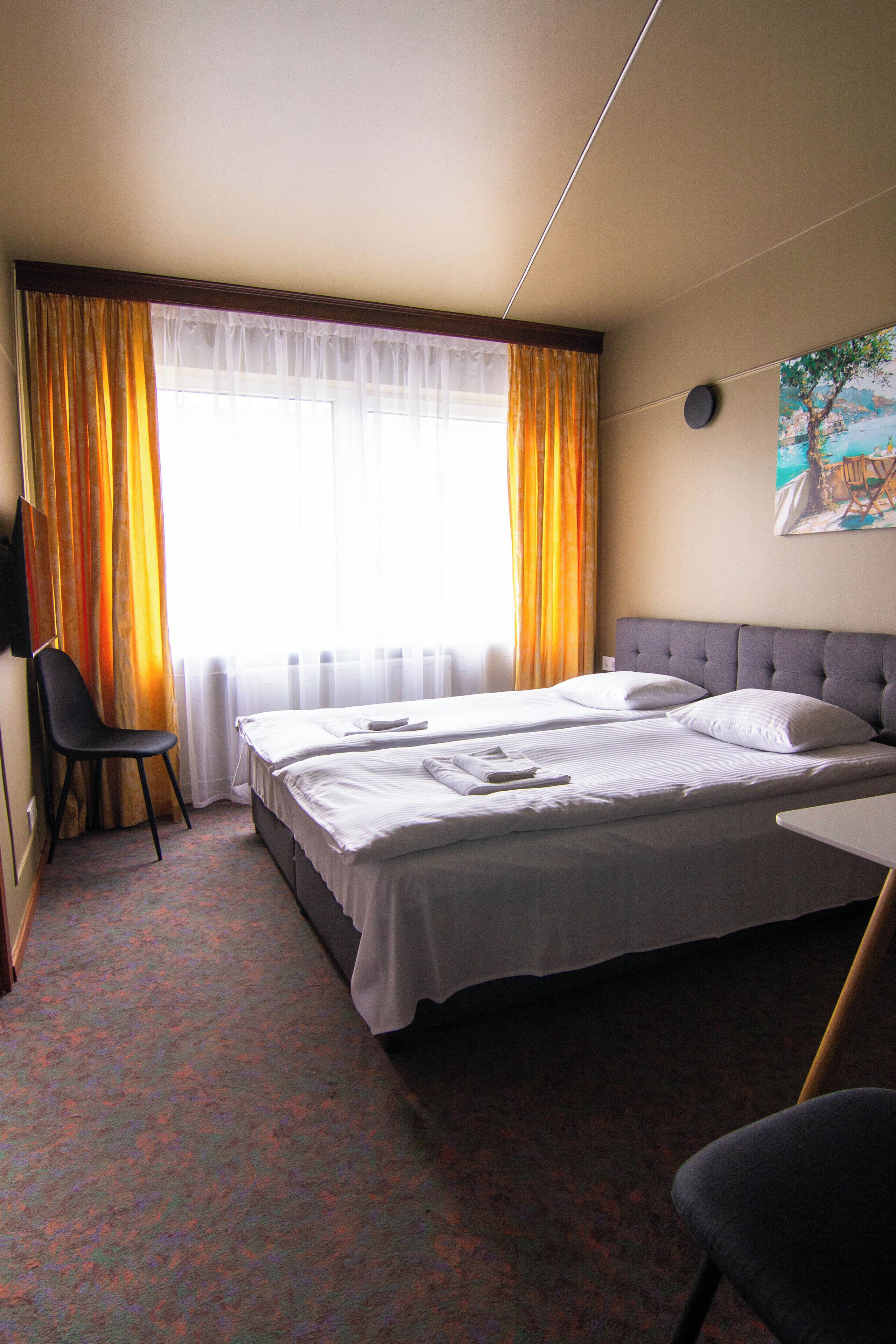 A hotel room with a bed, a chair, a desk, and a painting on the wall.