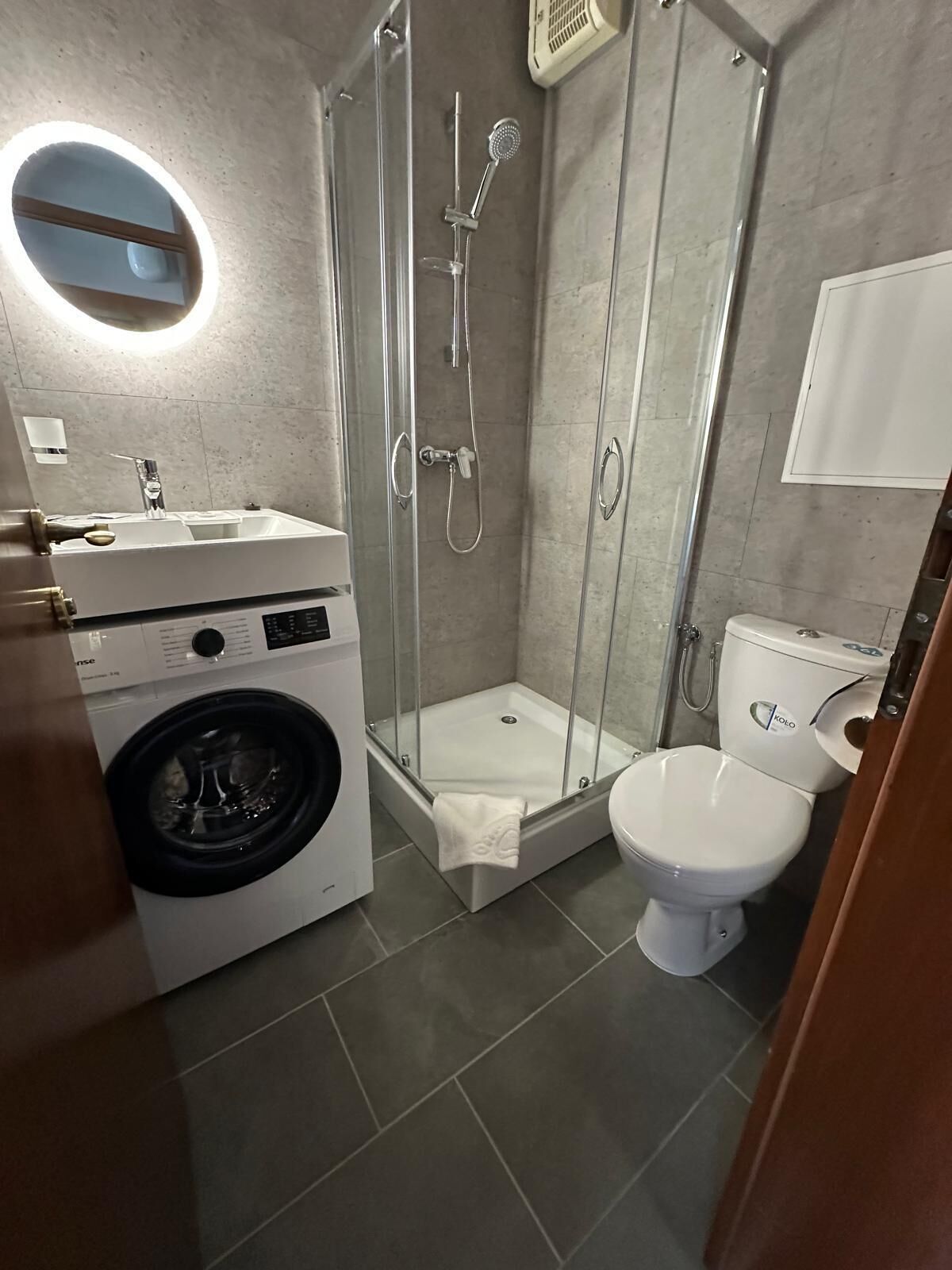 A modern bathroom with a glass-enclosed shower, a washing machine, a toilet, and a sink.