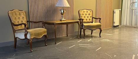 A lobby with two upholstered armchairs, a small table with a lamp, and a wall with vertical slats.