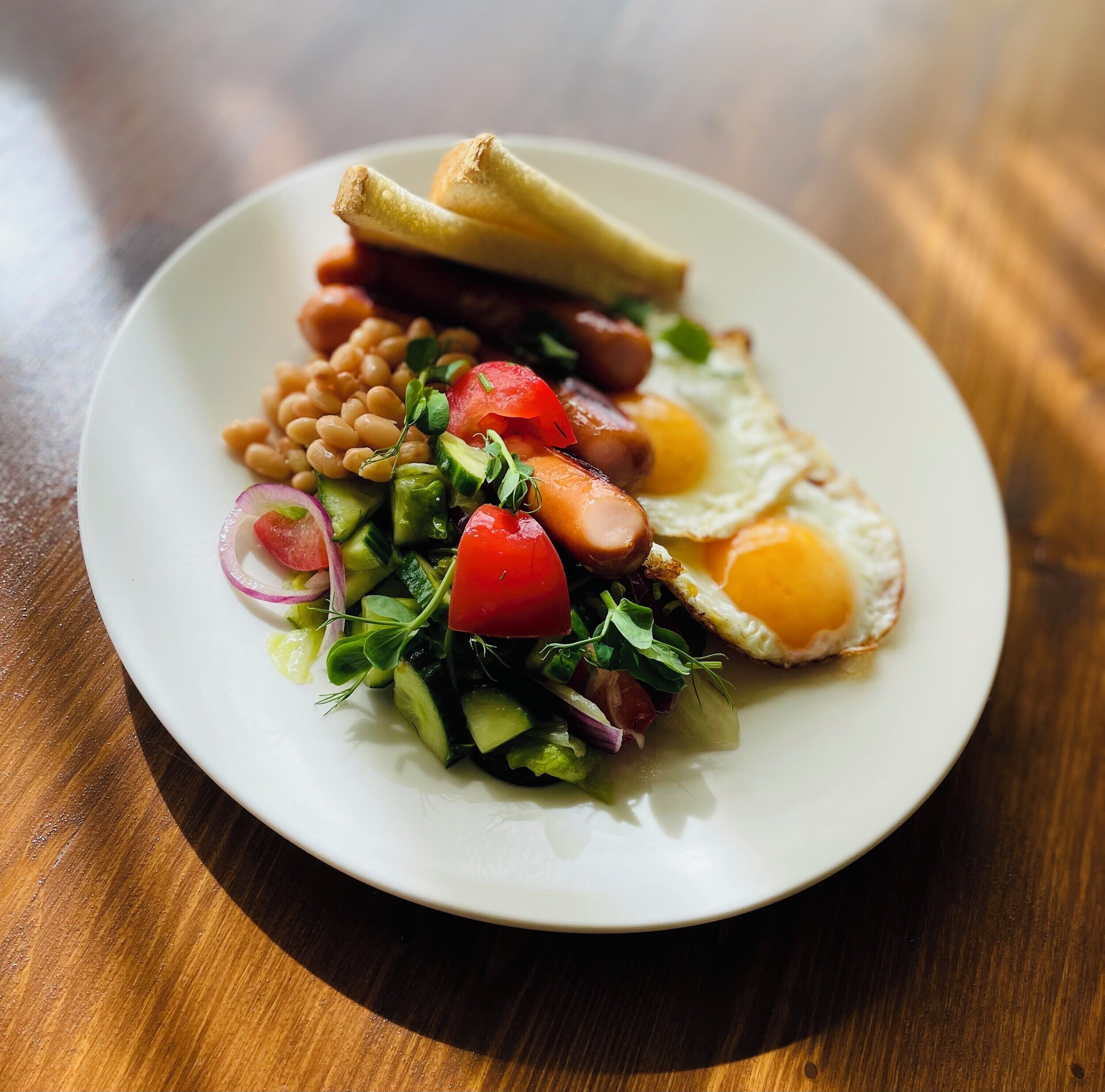 A plate of food with a fried egg, beans, tomatoes, and a salad.