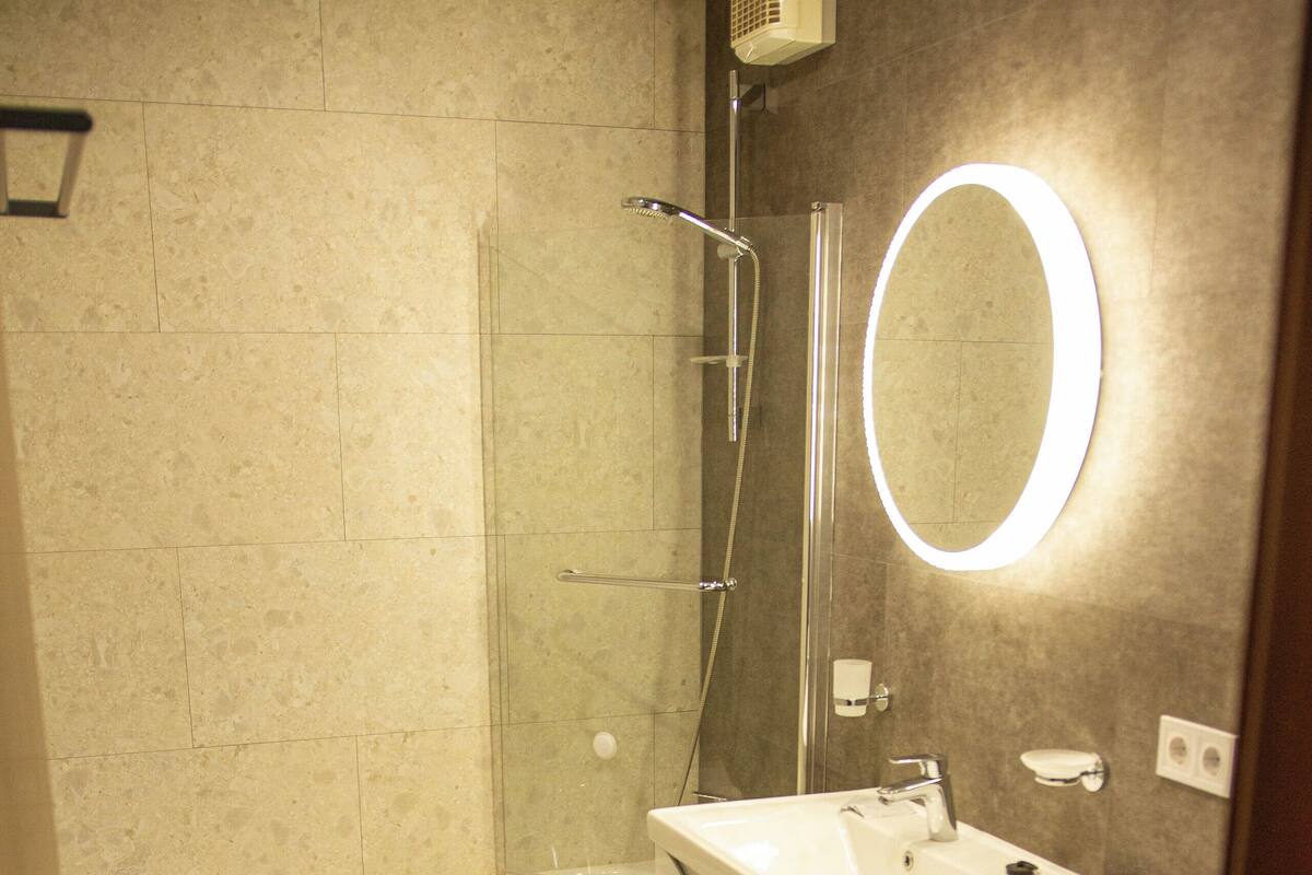 A bathroom with a bathtub, a washing machine, a toilet, and a mirror with a light.