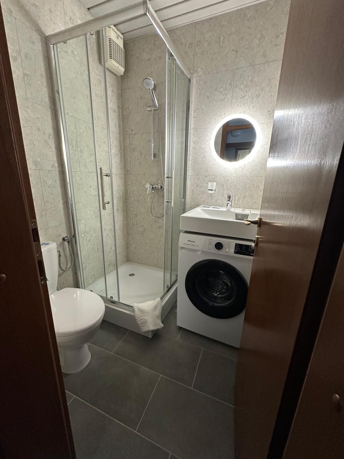 A compact bathroom with a glass-enclosed shower, a toilet, and a front-loading washing machine.