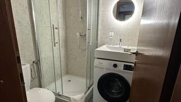 A compact bathroom with a glass-enclosed shower, a toilet, and a front-loading washing machine.