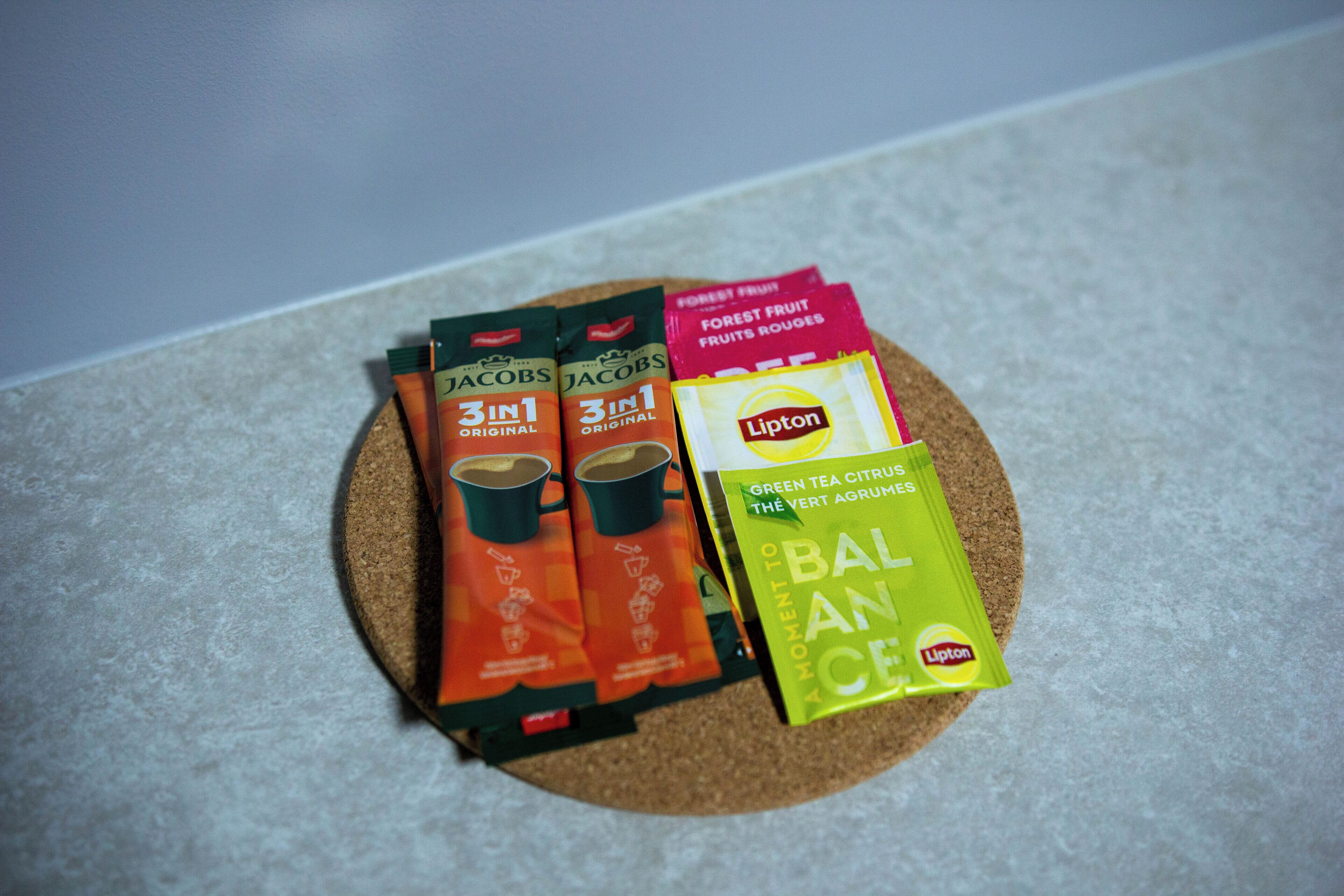 A cork coaster with four tea bags: Jacobs 3 in 1 Original, Jacobs 3 in 1 Forest Fruit, Lipton Green Tea Citrus, and Lipton Balance.