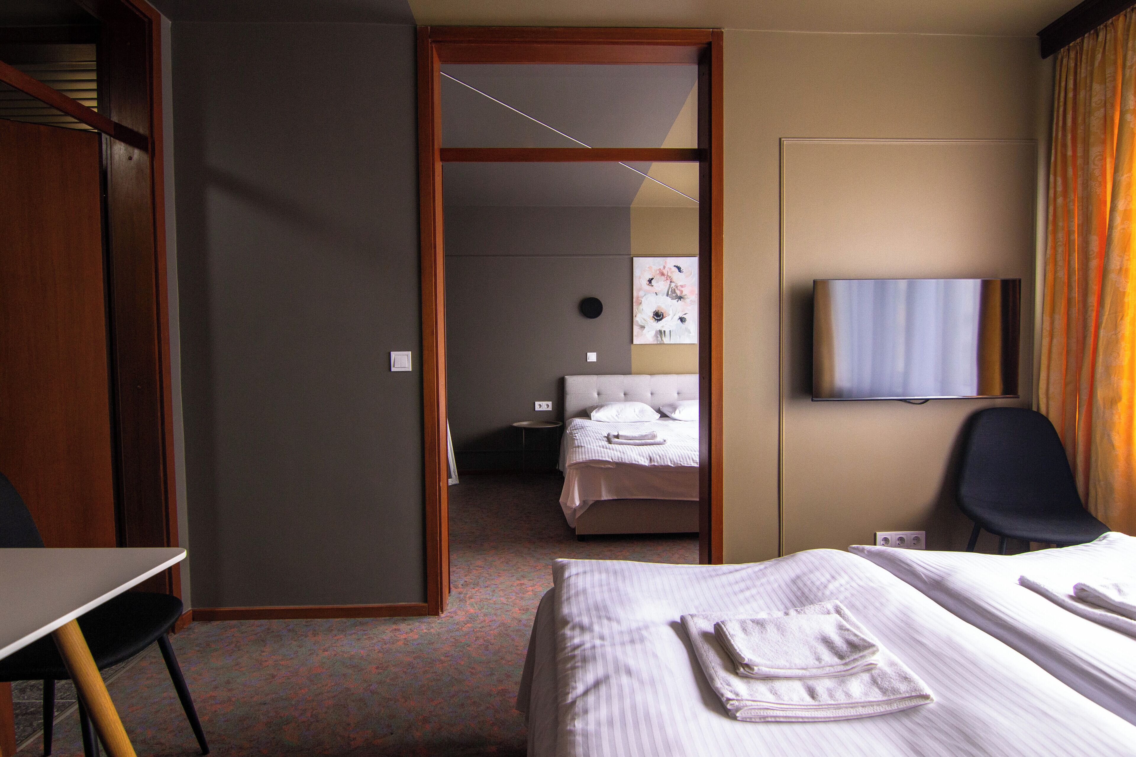 Habitación de hotel con cama, escritorio, silla, televisión y baño visible a través de una puerta abierta.