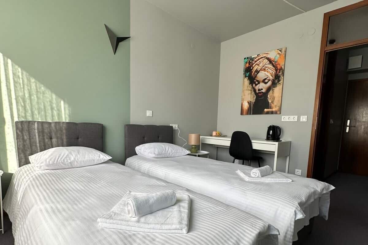 A hotel room with two beds, a desk, a chair, a coffee maker, and a painting on the wall.