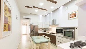 A modern kitchen with a glass dining table, stainless steel appliances, and a framed sign on the wall.