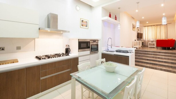 A modern kitchen with a gas stove, microwave, and oven, a glass dining table, and a red sofa in the living area.