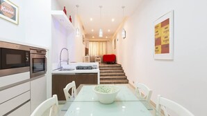 A modern kitchen with built-in appliances, a dining area with a glass table, and a staircase leading to a living area.