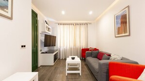 A modern living room with a grey sofa, red armchairs, a flat-screen TV, and a small white table.