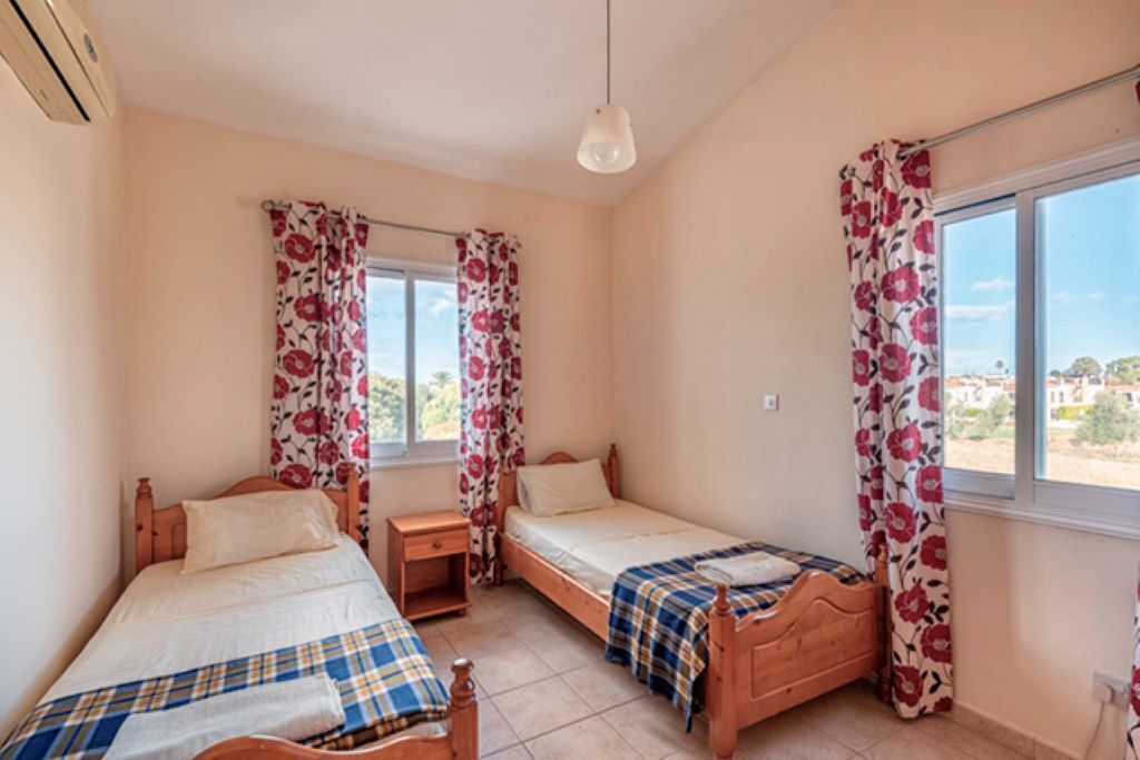 A bedroom with two wooden beds, a window with floral curtains, and a view of the outside.
