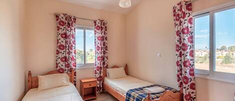 A bedroom with two wooden beds, a window with floral curtains, and a view of the outside.