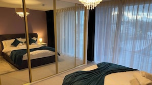 A hotel room with a large mirror, a bed with a dark headboard, a chandelier, and sheer curtains. - The Penthouse in Norfolk (Norwich)