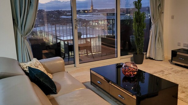 A modern living room with a large window, a sofa, a coffee table, and a potted plant. - The Penthouse in Norfolk (Norwich)