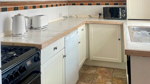 A kitchen with white cabinets, a microwave, a stove, and a tiled backsplash. - Charming Brighton Townhouse (Brighton and Hove)