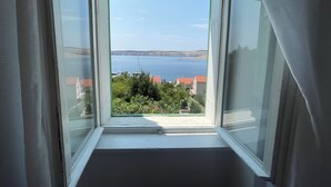 A room with a large window offering a view of the sea and a distant coastline. - Apartment Perovic (Jadranovo)