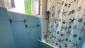 A bathroom with blue tiles, a shower curtain with sea creature prints, and a blue bath mat. - Apartment Perovic (Jadranovo)