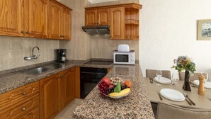 Una cocina con gabinetes de madera, encimeras de granito, microondas, cafetera y un bol de frutas.