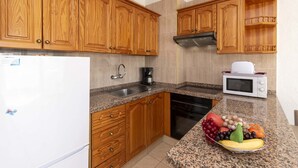 Una cocina con armarios de madera, un lavaplatos de acero inoxidable, un microondas y un frutero en la encimera.
