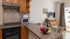 Una cocina con encimeras de granito, armarios de madera, microondas, estufa y comedor con una mesa para dos.