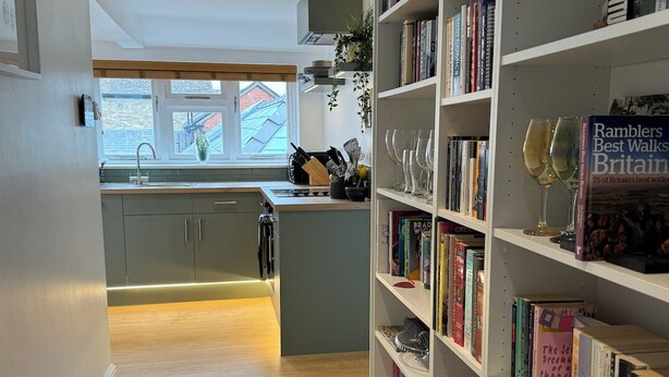 A modern kitchen with a view to the outside, a bookshelf filled with books, and a carpeted floor.