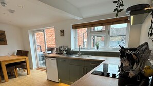 A modern kitchen with a wooden dining table, a built-in dishwasher, and a window overlooking a brick building.