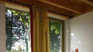 Un lit simple dans une chambre avec une fenêtre, un rideau et un luminaire fixé au mur.
