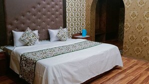 Un dormitorio con una cama grande, piso de madera y papel tapiz estampado.