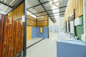 Une salle de bain avec des cloisons en bambou, un ventilateur de plafond et deux lavabos avec miroirs.
