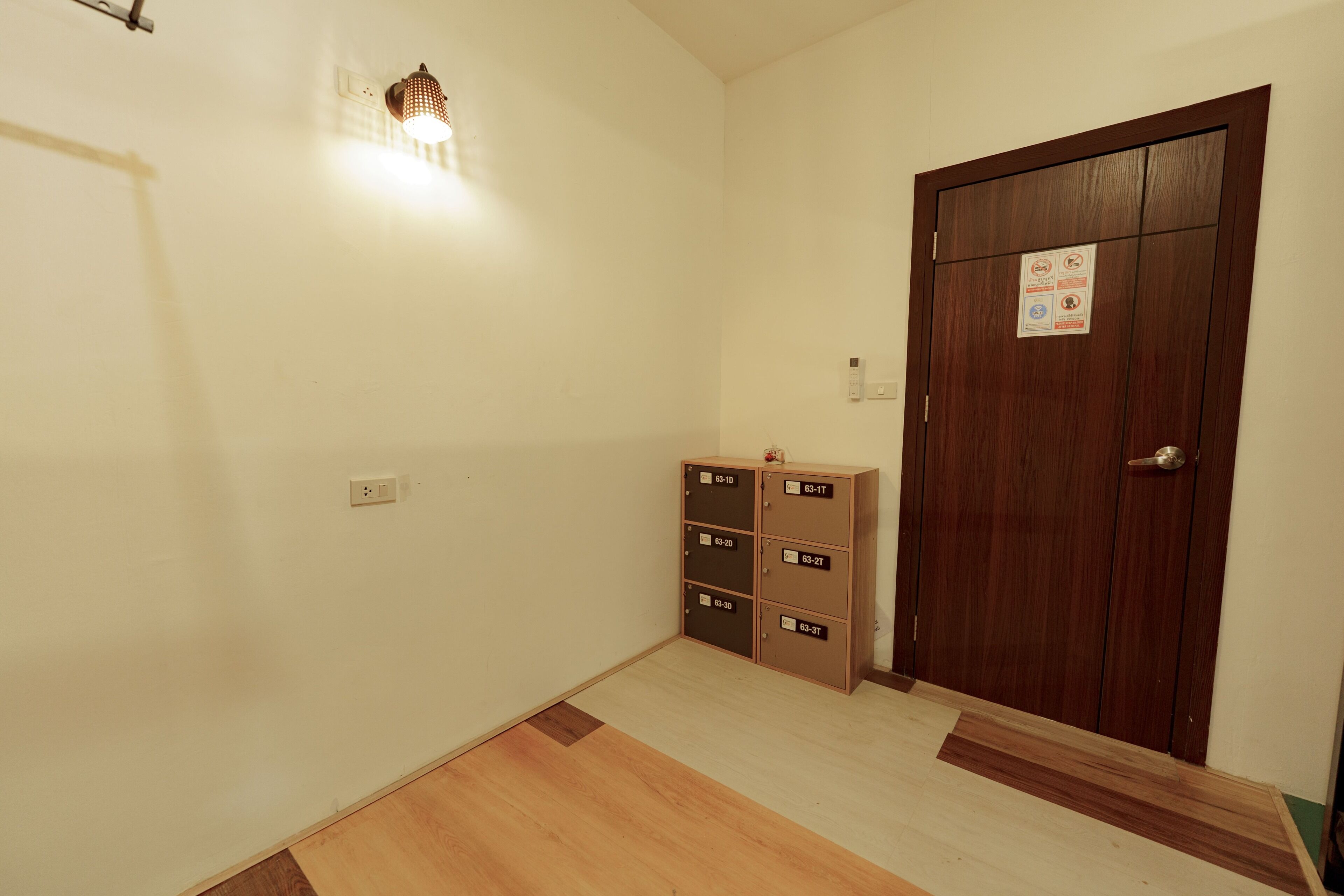 A room with a wooden floor, a door with a sign, and a wall-mounted light fixture.