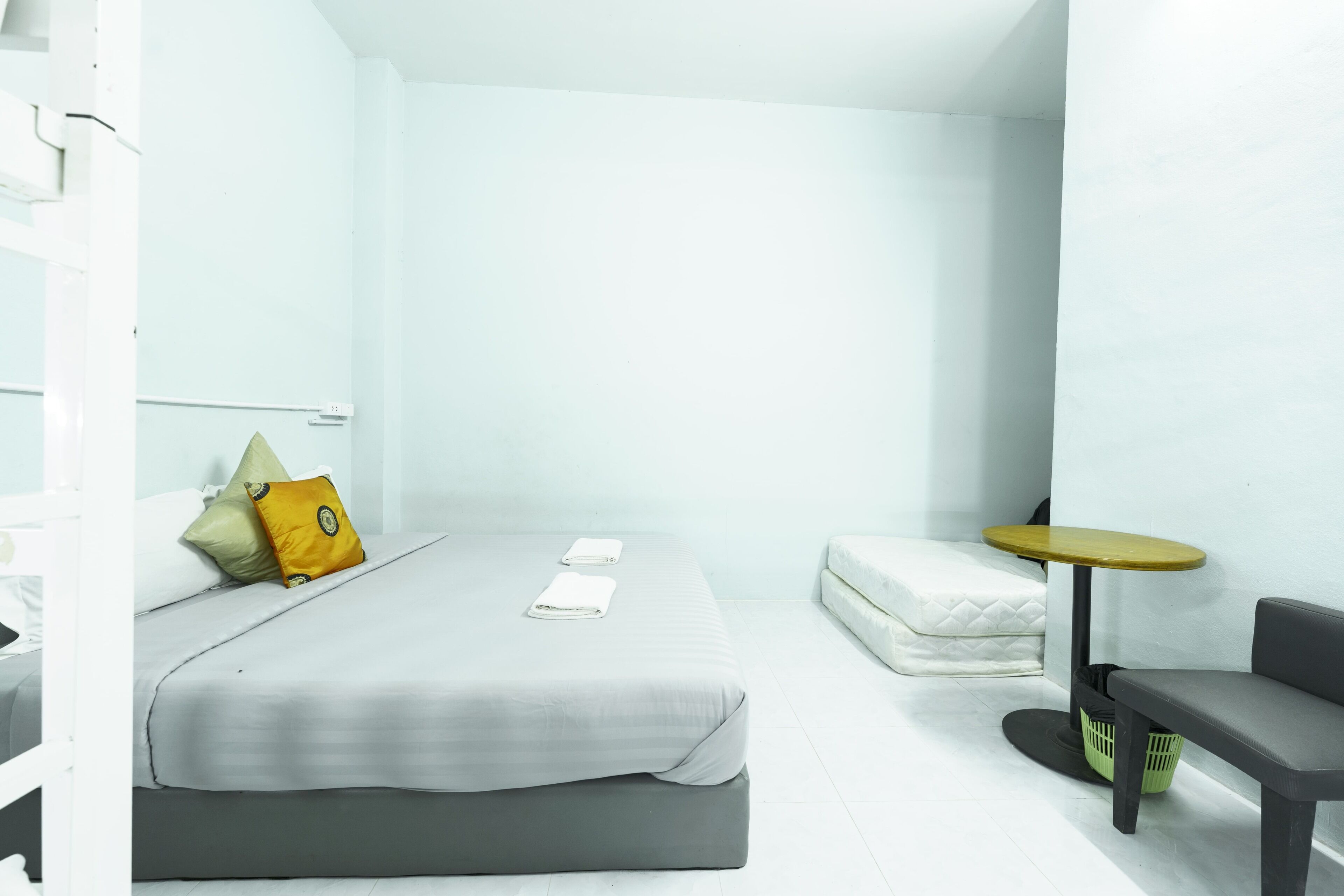A modern hotel room with a bed, a small table, a bench, and a mattress on the floor.