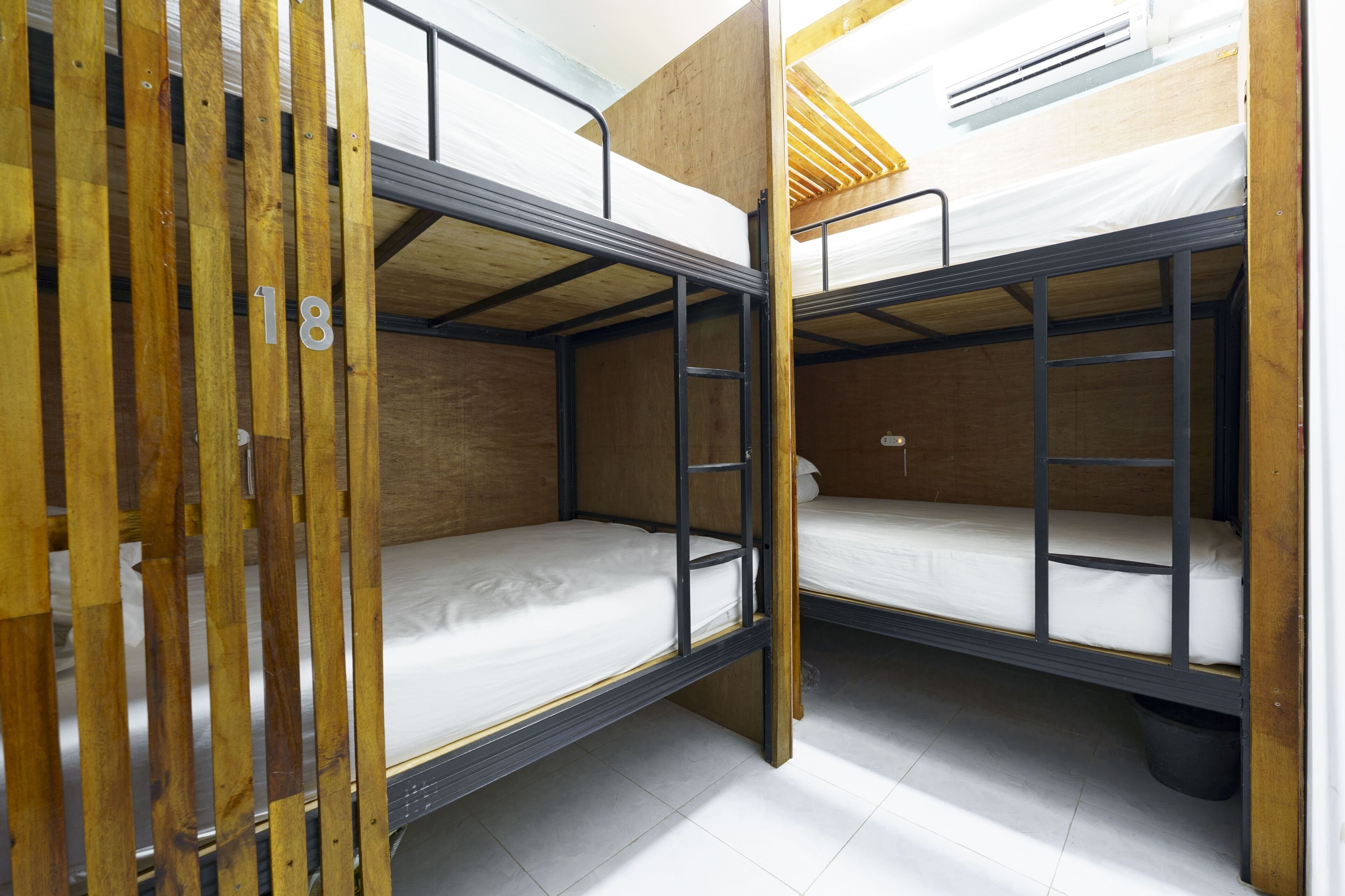 A bunk bed room with wooden slats, numbered 18, and a metal ladder.